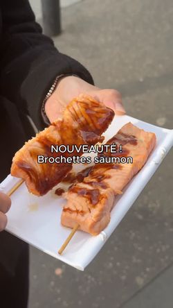 Brochettes de saumon grillé nappées de sauce, servies sur une assiette blanche dans un restaurant japonais.