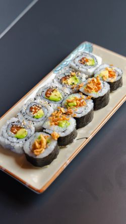 Sushis variés sur un plat, incluant des makis au thon et à l'avocat, décorés de croustillants.