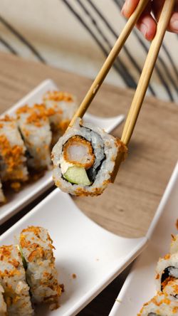 Restaurant japonais proposant des california rolls avec crevette tempura, avocat, et fromage, servis sur plateaux blancs.