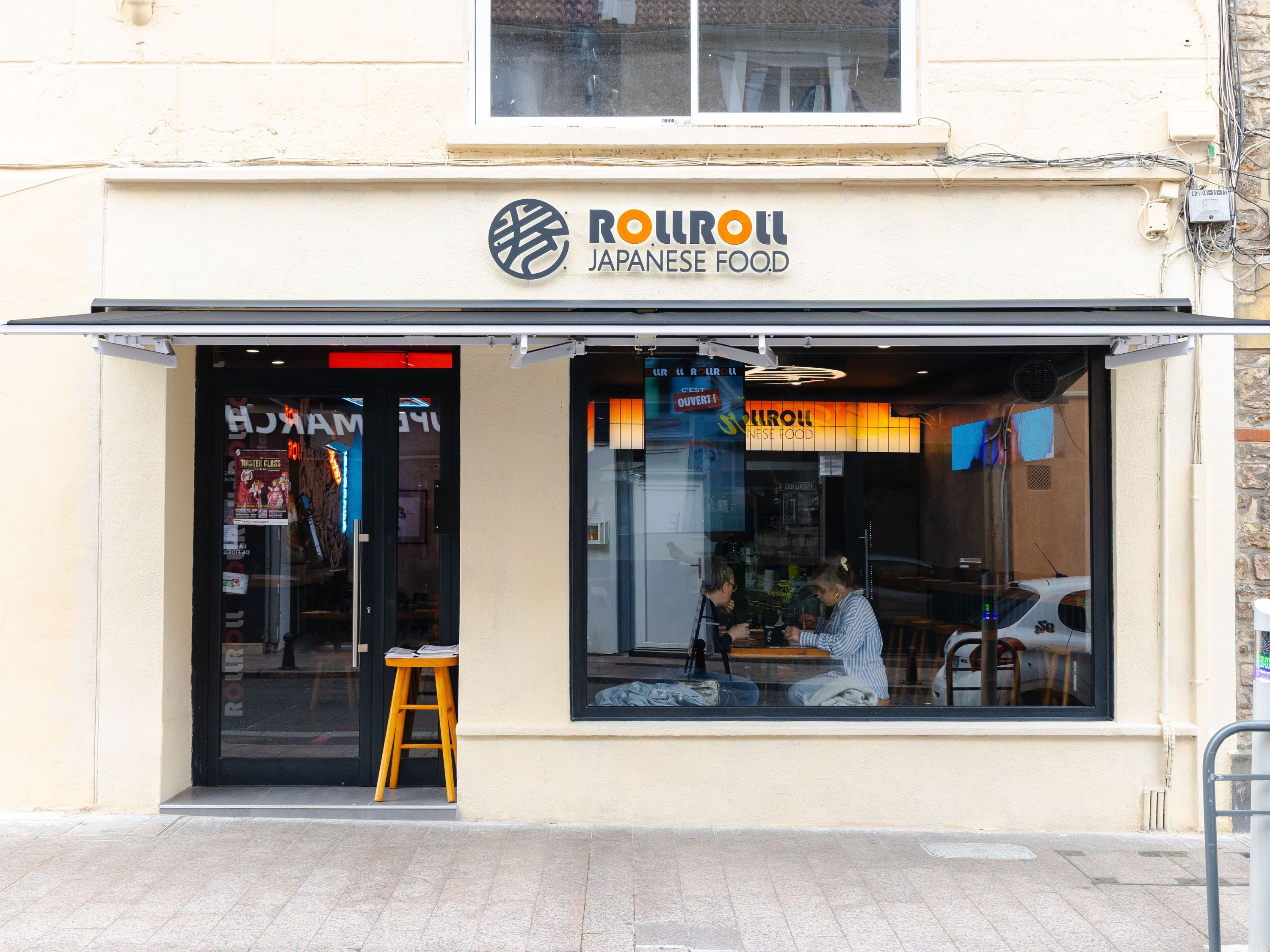 Façade de Rollroll Palaiseau Japanese Food avec une grande vitrine et un store noir ouvert sur rue piétonne.