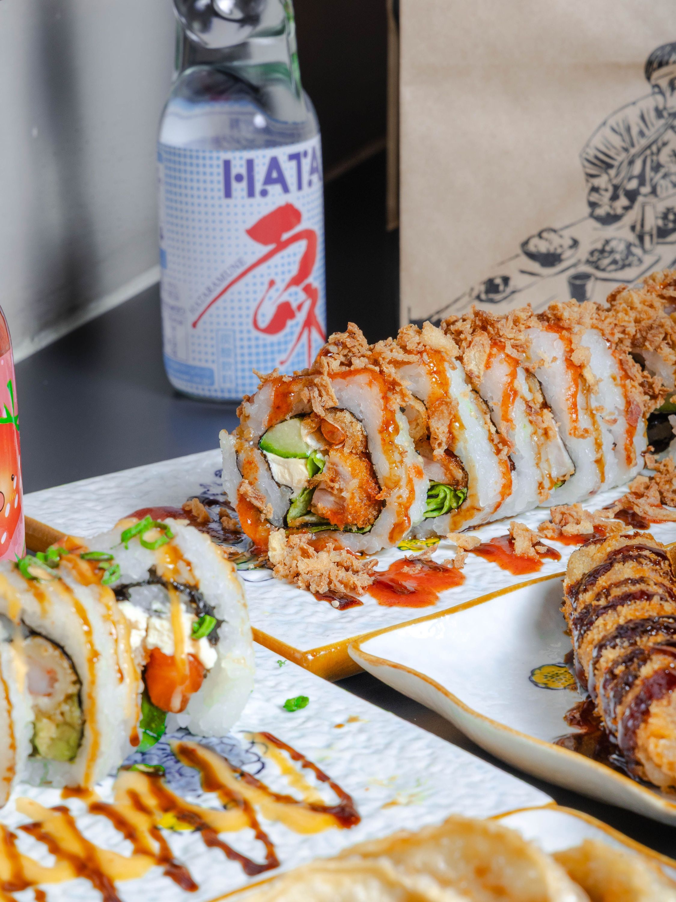 Rouleaux de sushi variés avec sauces sur assiettes blanches, bouteille de boisson japonaise en arrière-plan.