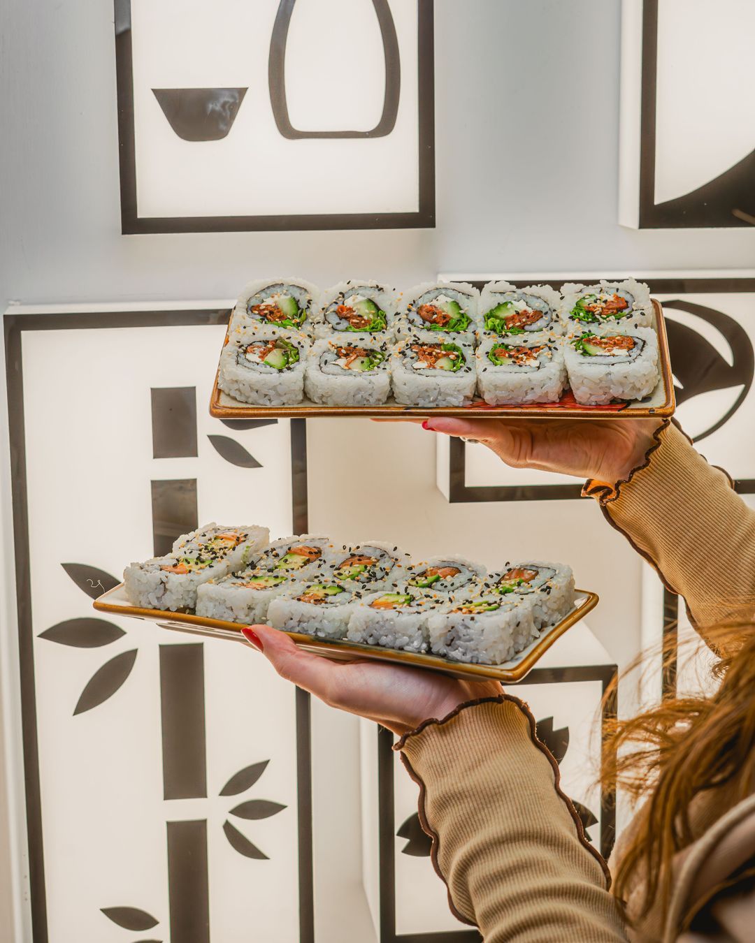 Sushi et maki présentés sur des plateaux, sur fond décoratif clair.