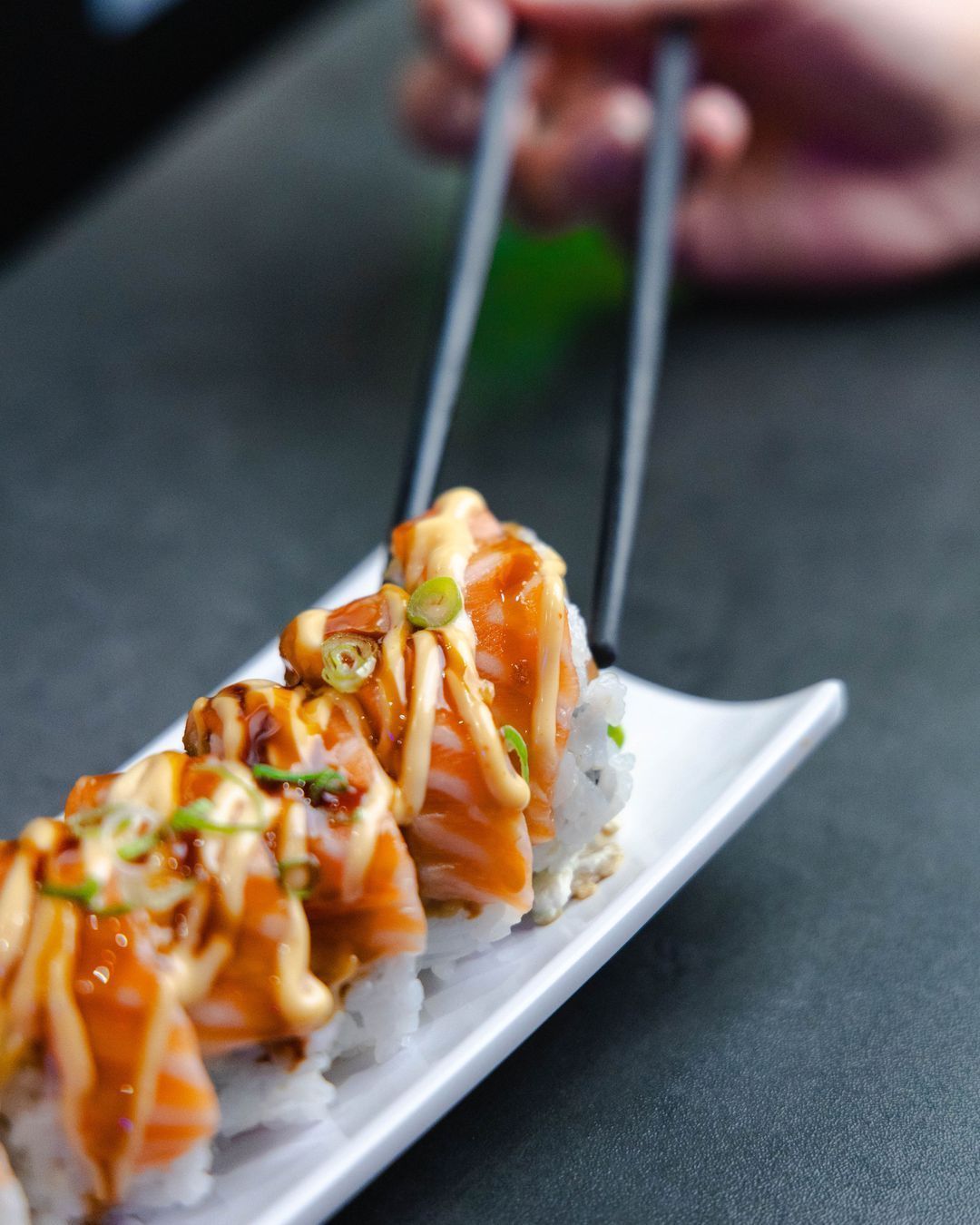 Assiette de sushi garnis de saumon et de sauce, présentée avec des baguettes.