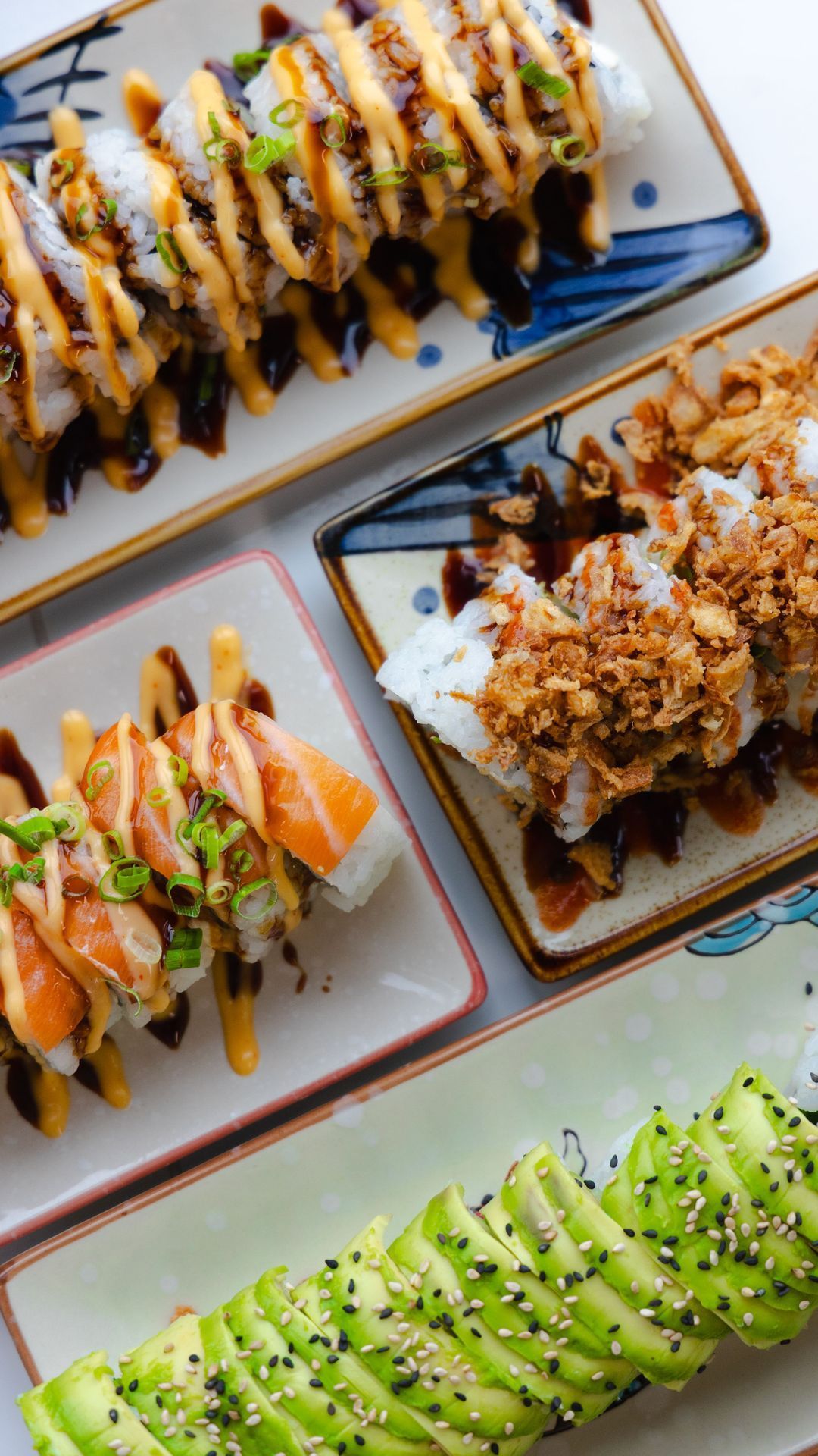 Assortiment de sushis incluant des rolls garnis de saumon, avocat et sauce, présenté sur des assiettes.