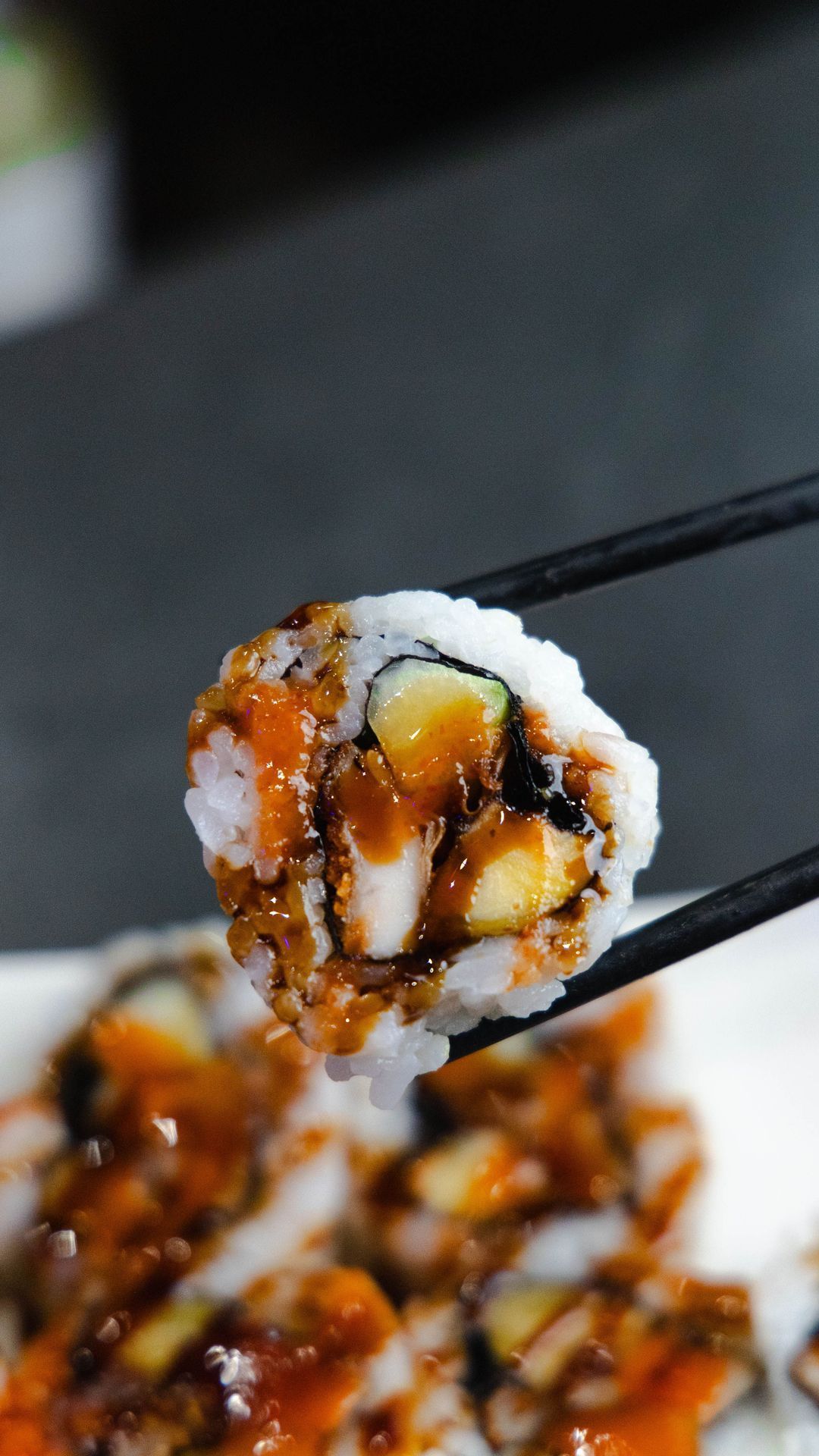 Maki japonais avec des ingrédients variés, servi avec une sauce sucrée sur le dessus.