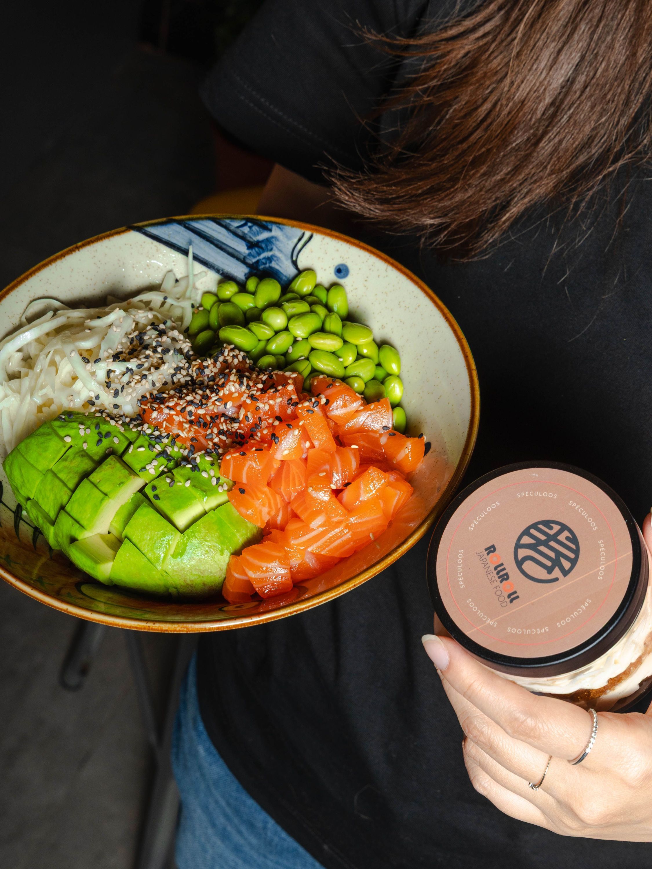 Bol de restaurant japonais contenant avocat, saumon, edamame et gingembre mariné, tenu à la main.