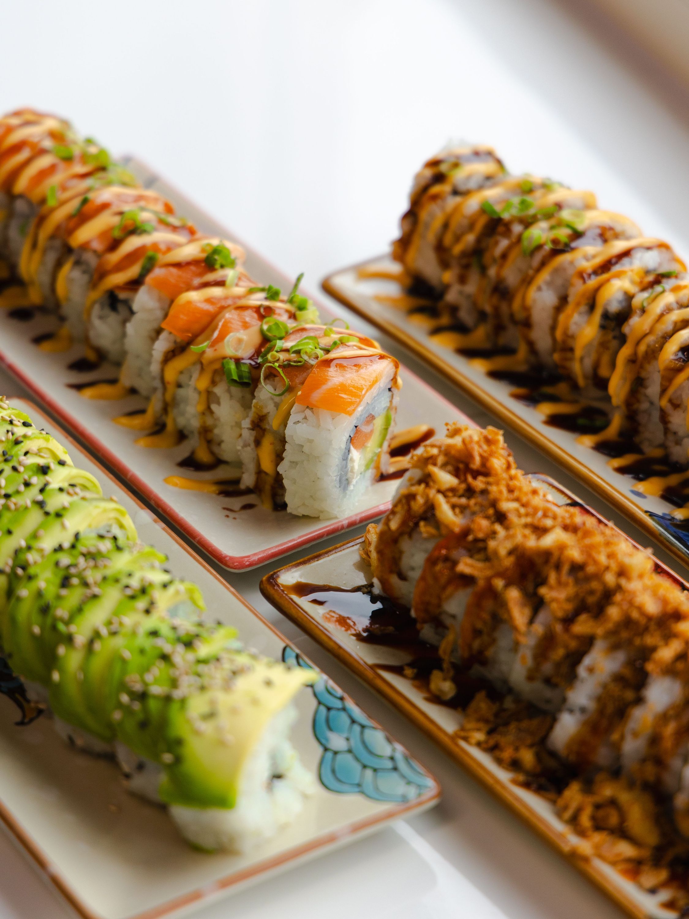 Rouleaux de sushi variés avec avocat, saumon et garnitures croustillantes présentés sur des assiettes rectangulaires.