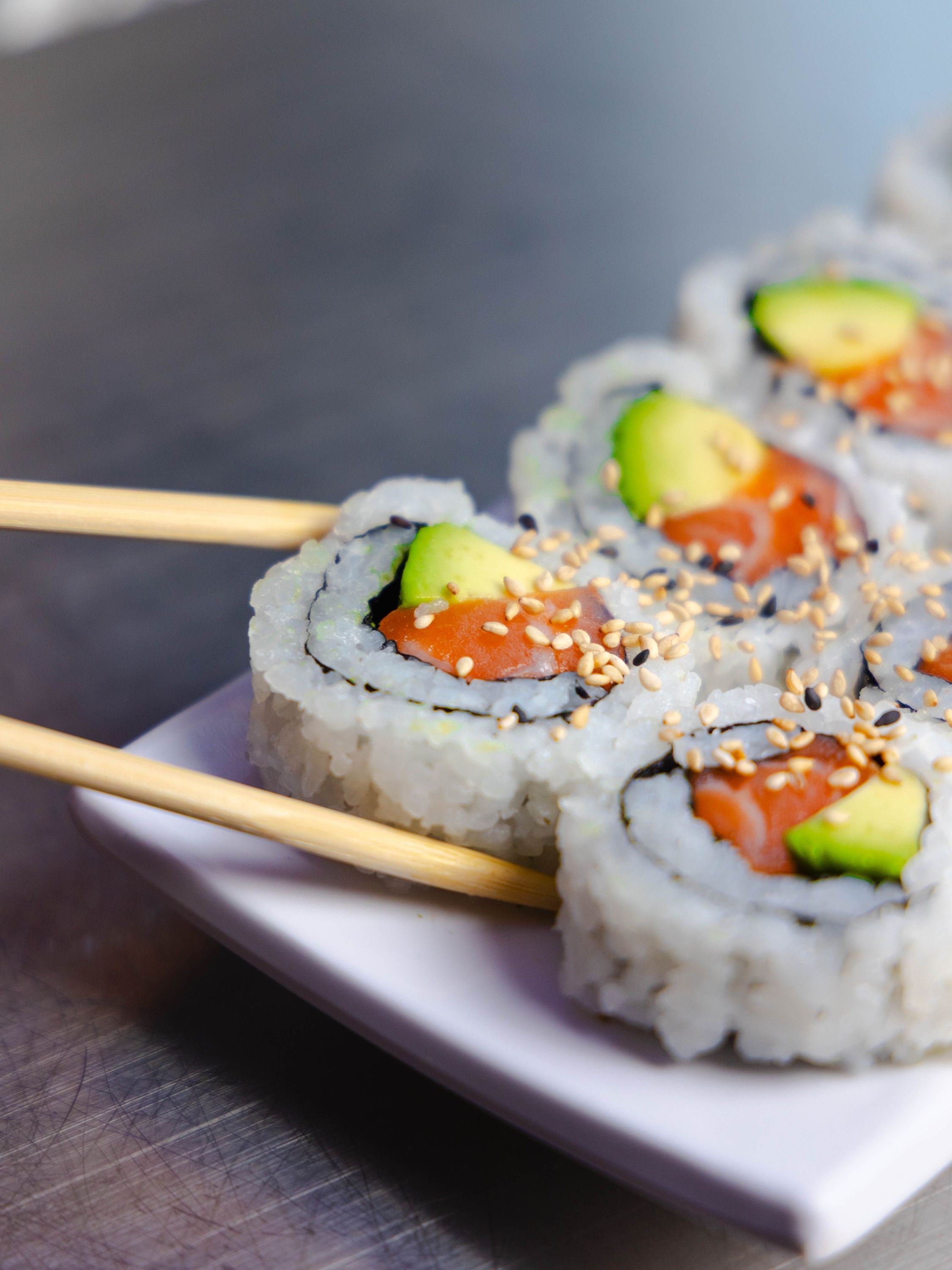 Sushis California rolls avec avocat et saumon, parsémés de graines de sésame sur une assiette blanche.