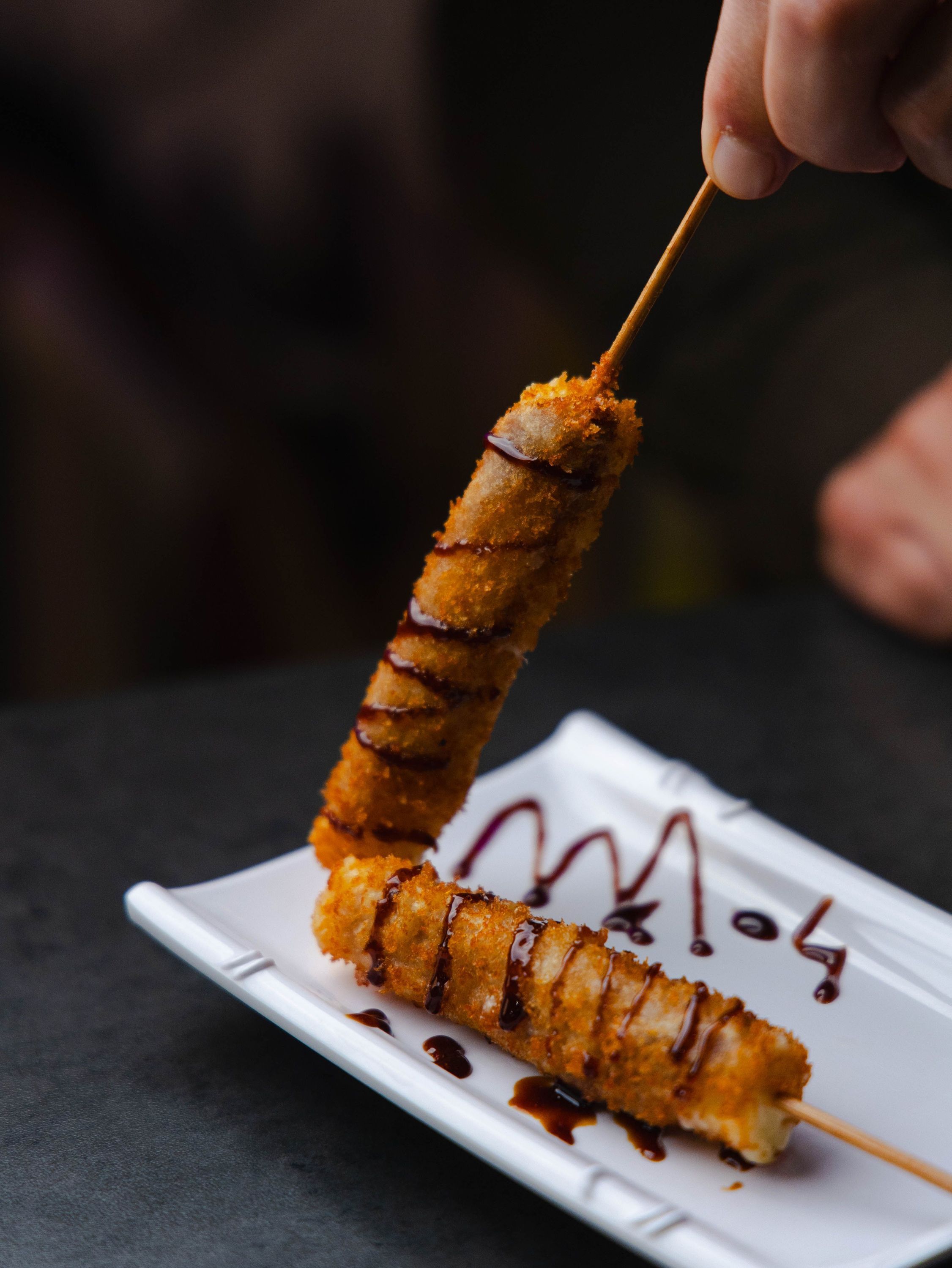 Brochettes frites nappées de sauce chocolat sur une assiette blanche, servies au restaurant japonais Rollroll.