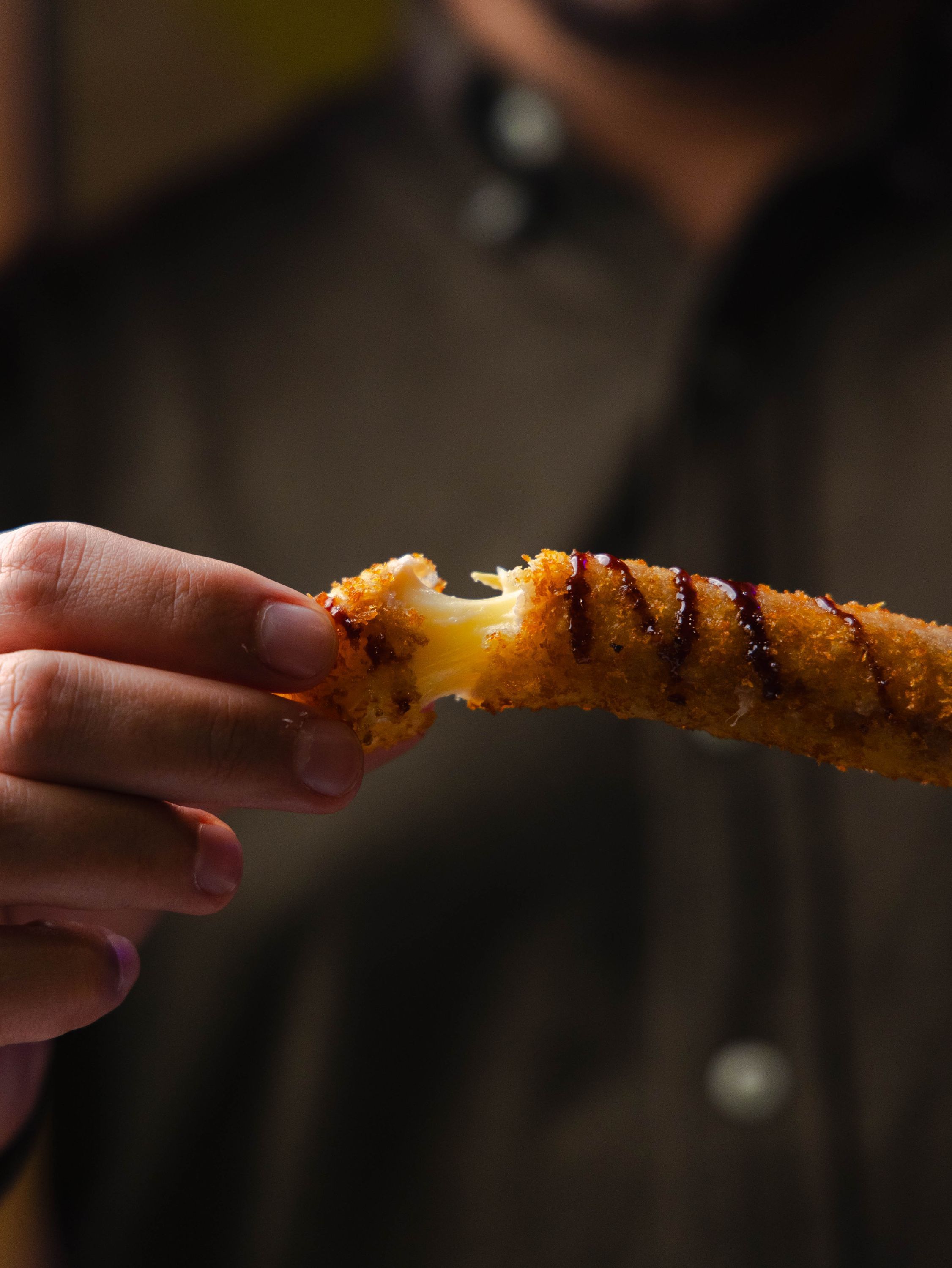 Un doigt de fromage pané, croustillant à l'extérieur, présenté sur une main, avec une sauce qui coule.