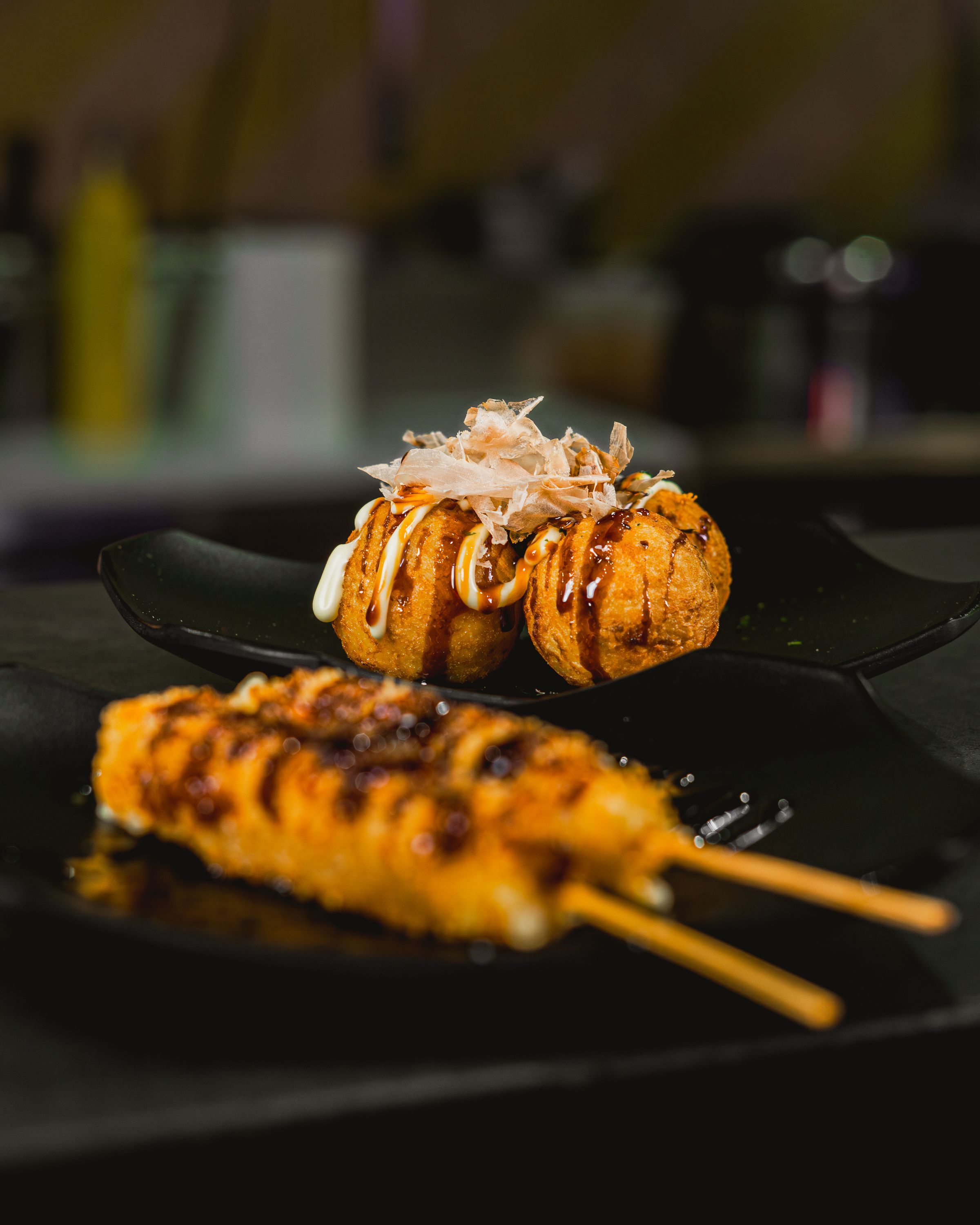 Plats japonais préparés, incluant des boulettes et brochettes, servis sur assiette noire.