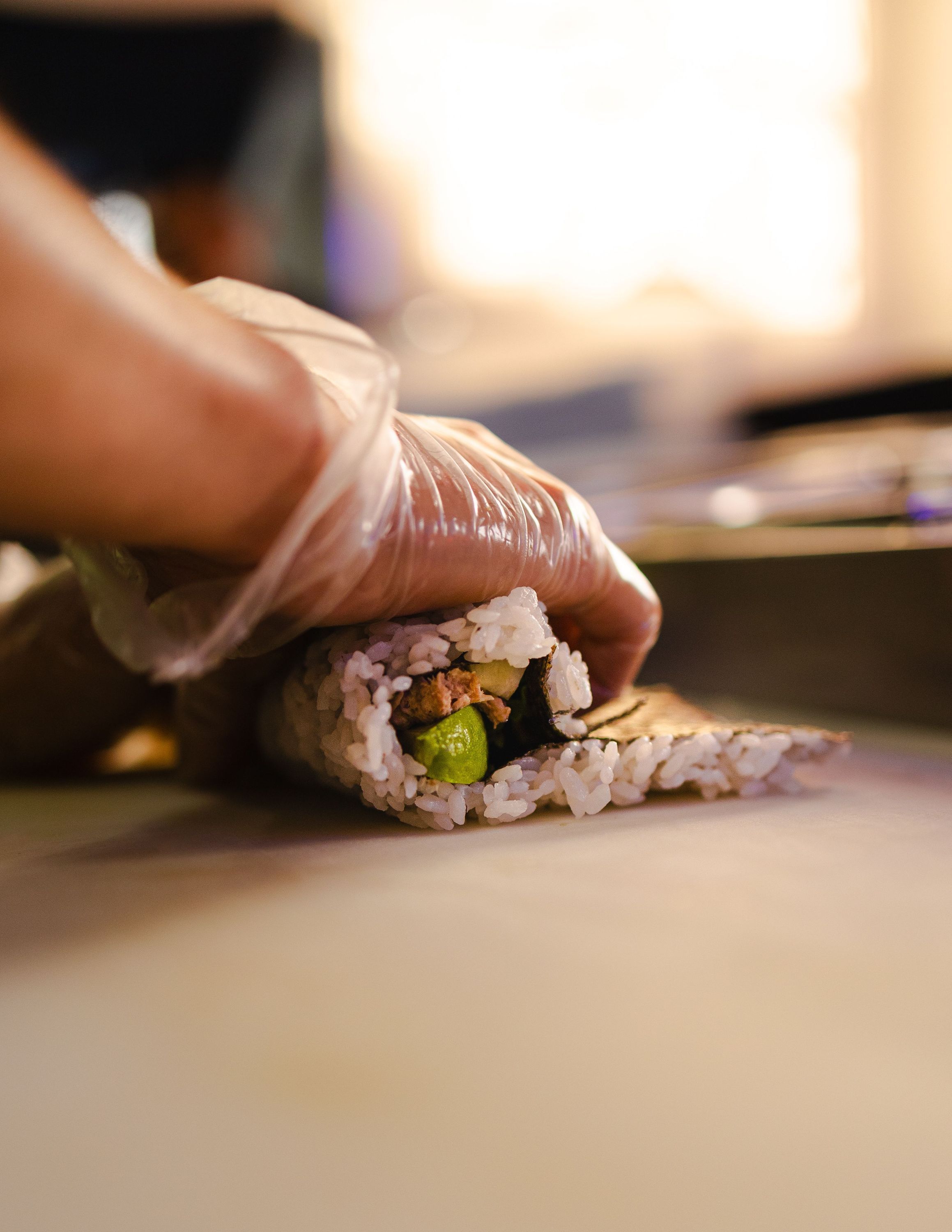 Préparation d'un maki dans un restaurant japonais avec des mains gantées en gros plan.