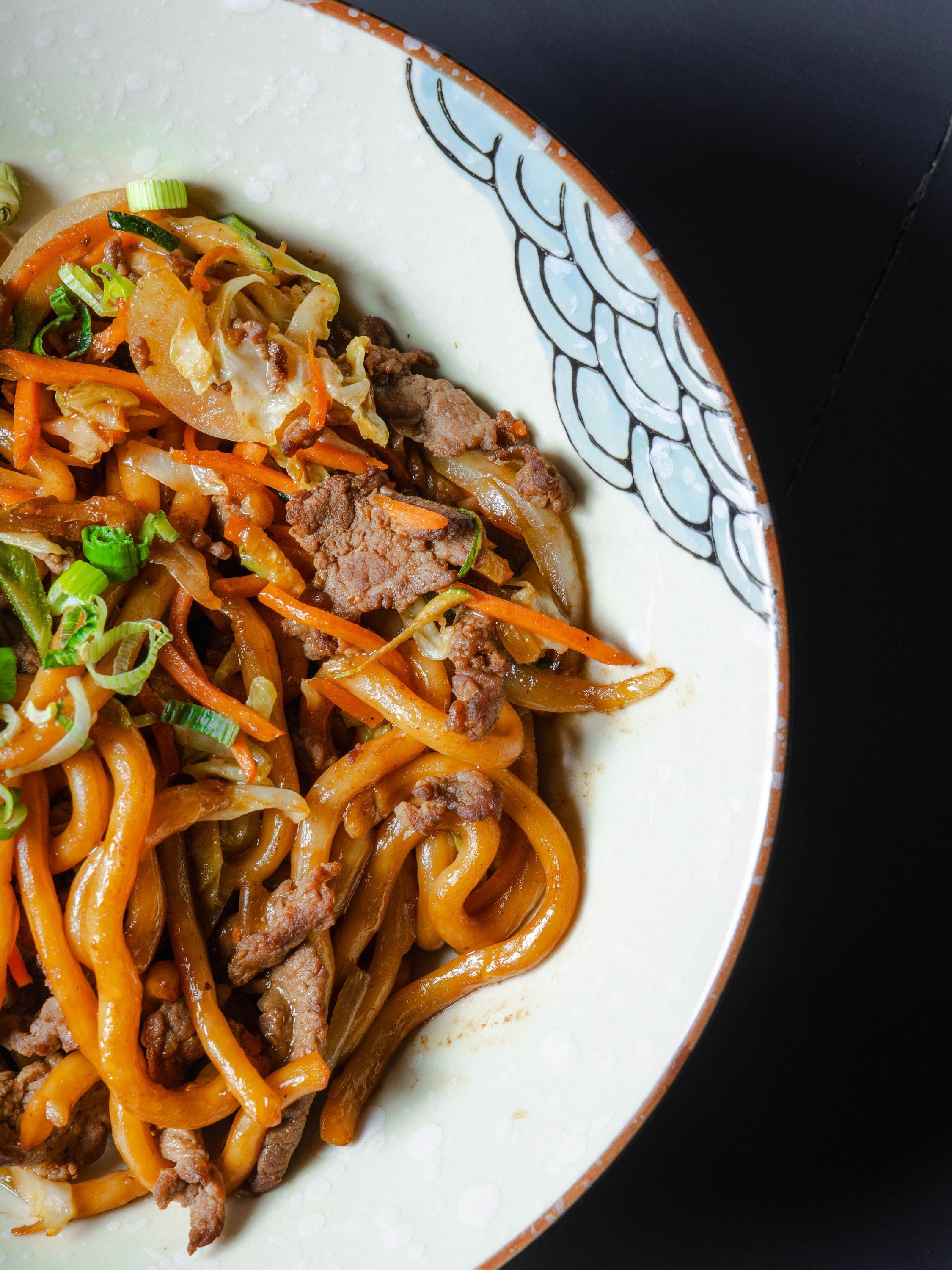 Plat japonais avec nouilles sautées, viande et légumes dans un bol décoré typique du restaurant Rollroll Vanves.