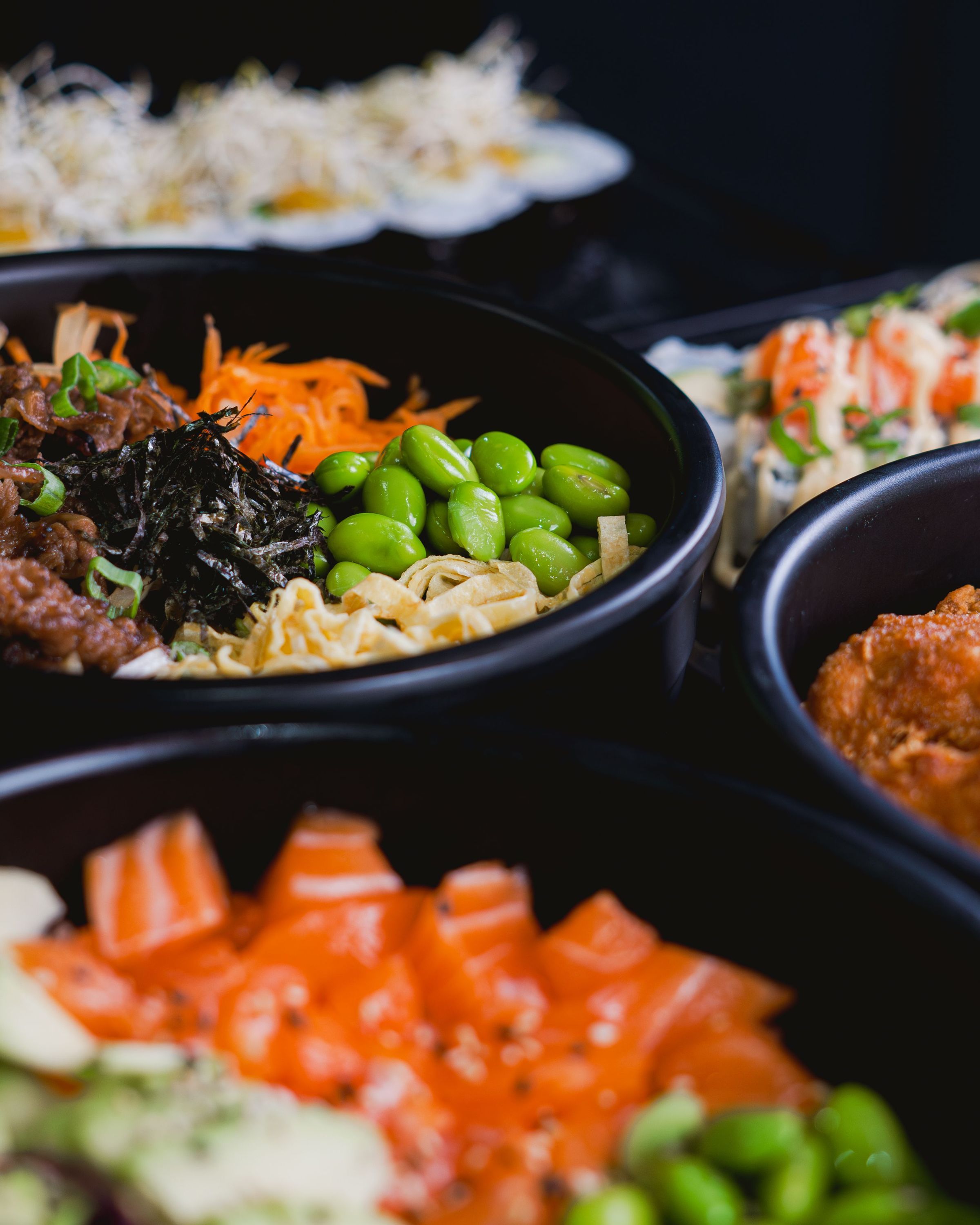 Plats japonais variés avec edamame, sashimi de saumon, et makis présentés en bols et assiettes.