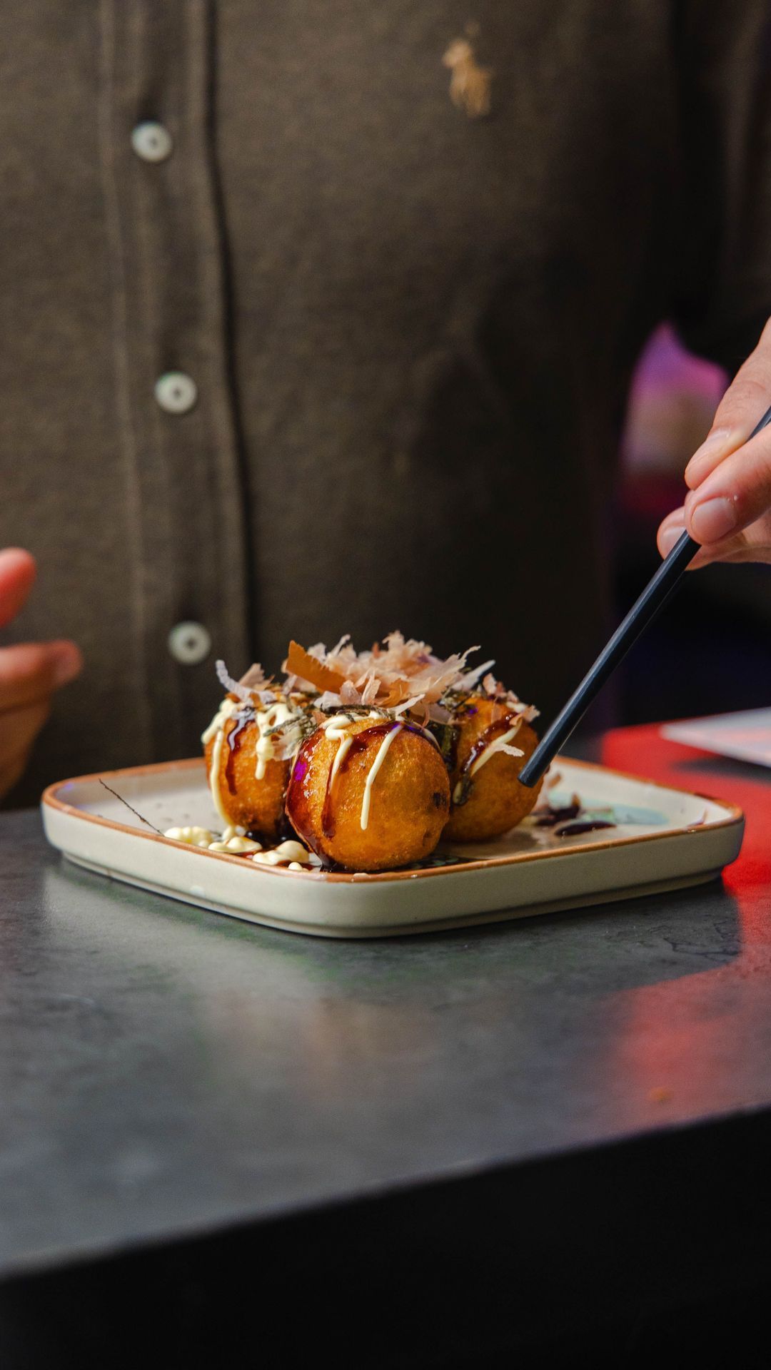Des boulettes japonaises garnies de sauce et de flocons de bonite servies d'une main sur une assiette.