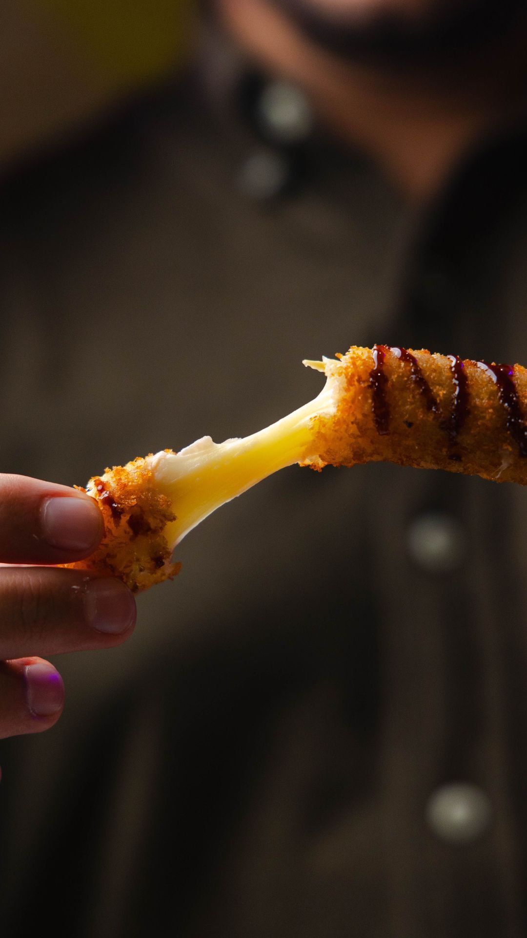 Une personne tient un bâtonnet croustillant avec du fromage fondant à l'intérieur, mettant en valeur un plat savoureux.