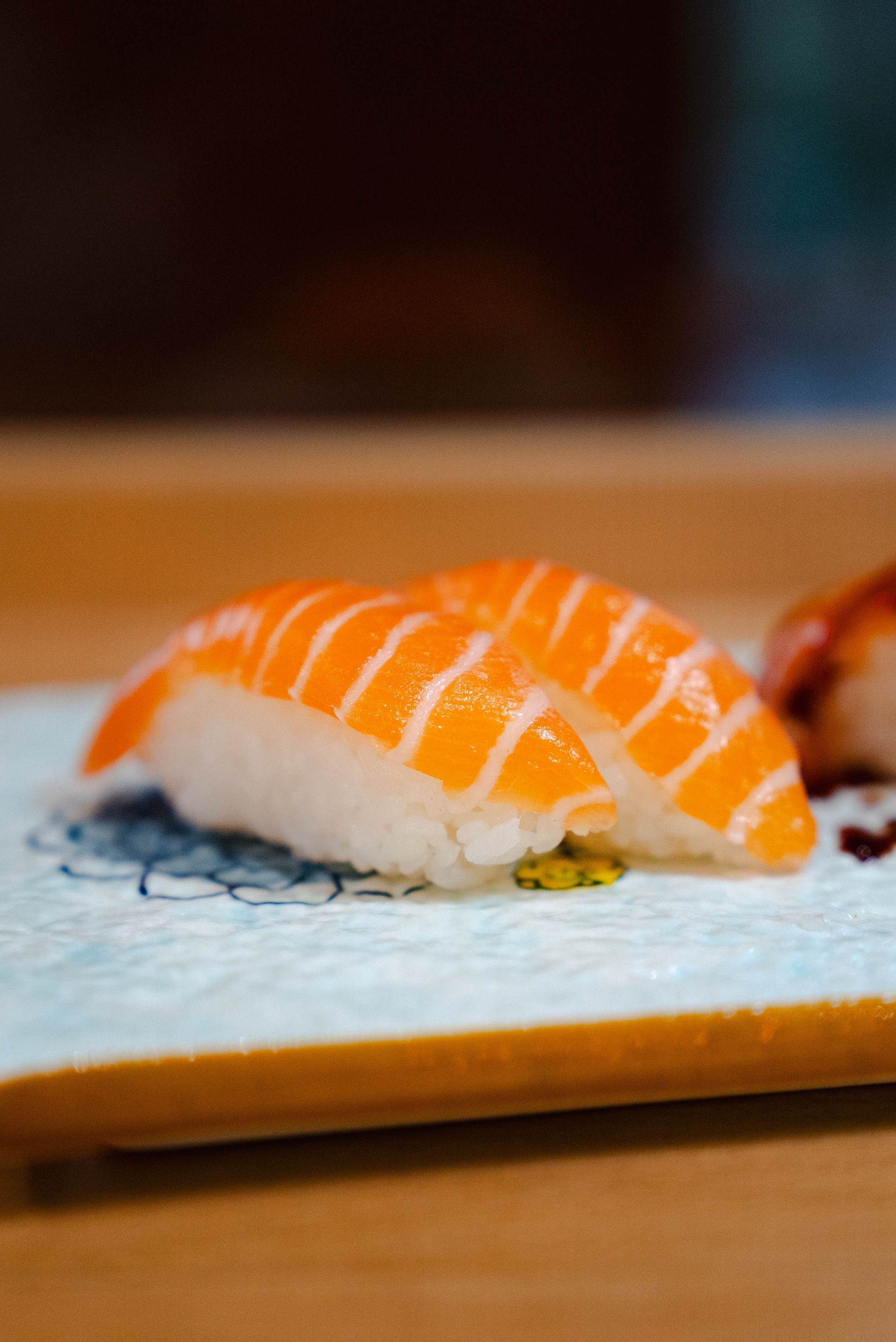 Deux pièces de sushi au saumon posées sur une assiette blanche avec motifs, spécialité du restaurant japonais.