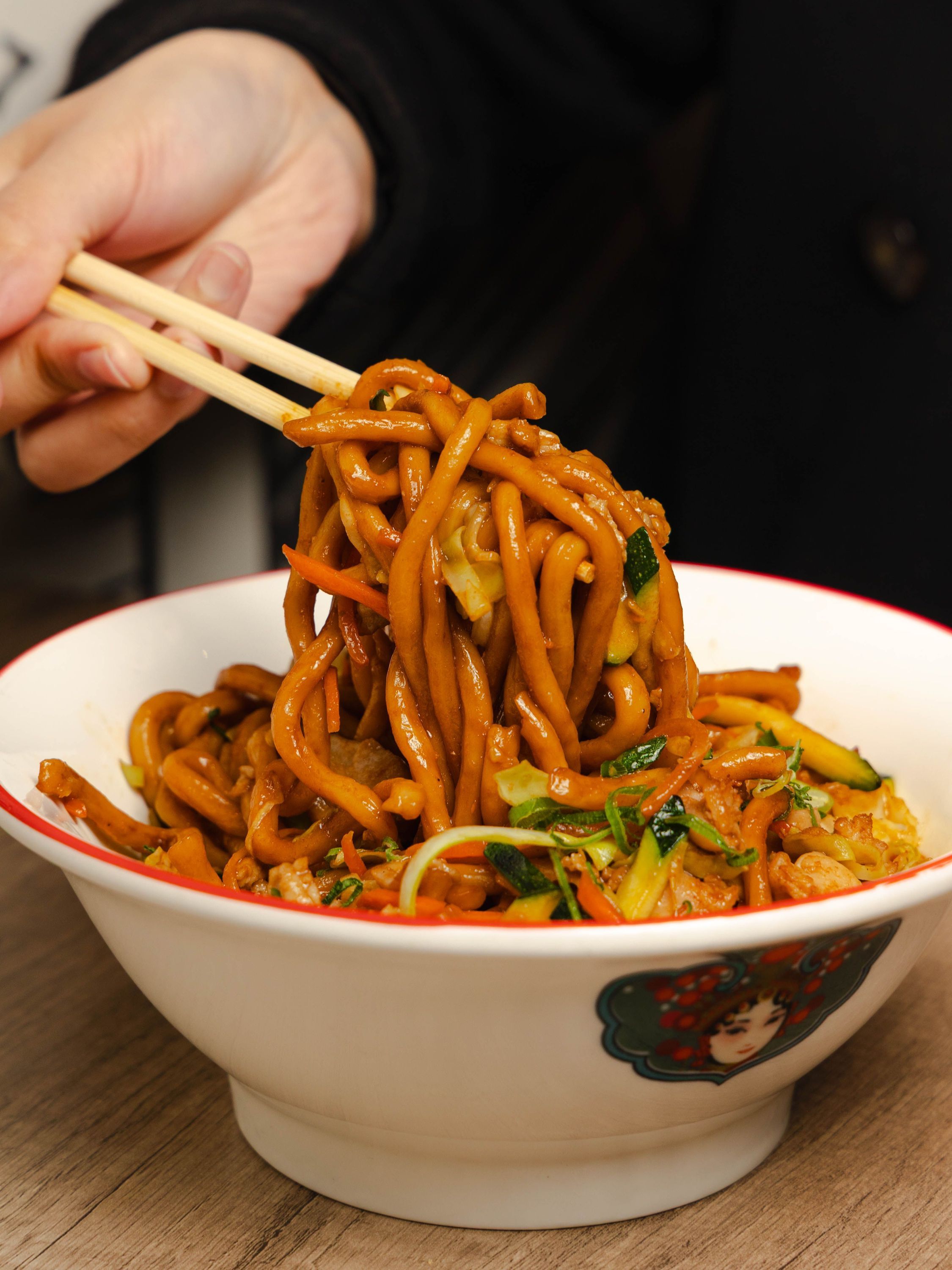 Nouilles sautées asiatiques servies dans un bol avec légumes et prise à l'aide de baguettes.