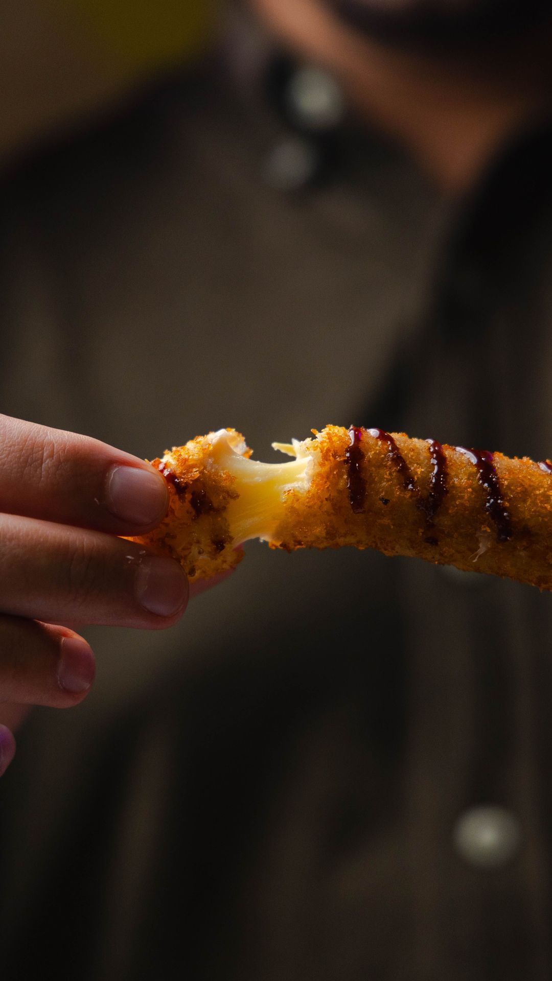 Un morceau de fromage enrobé de panure, tenu à la main, avec une sauce visible sur le dessus.