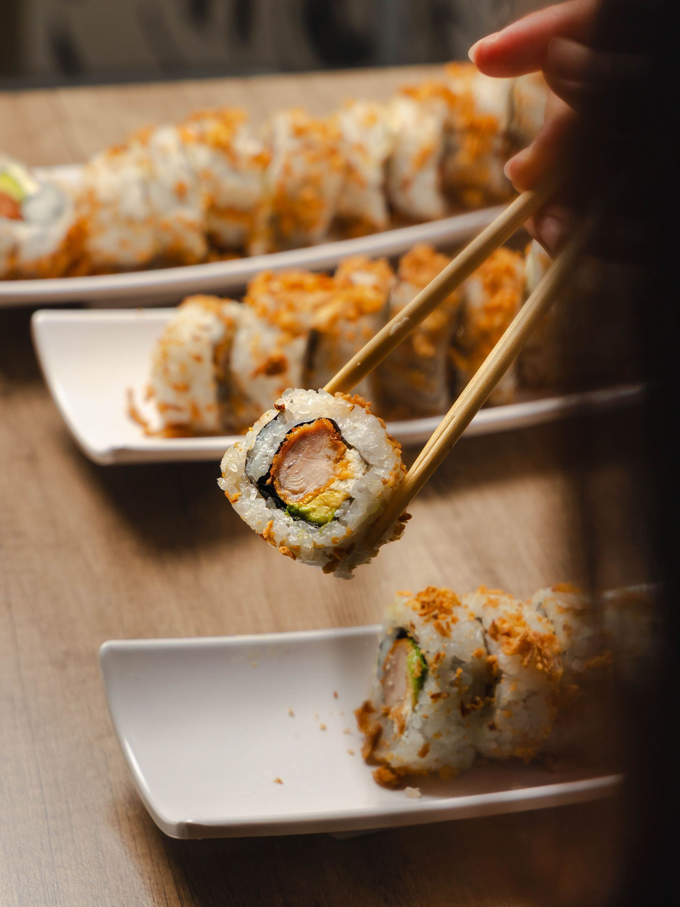 Maki japonais tenu avec des baguettes, présenté sur assiettes blanches dans le restaurant Rollroll Vanves.