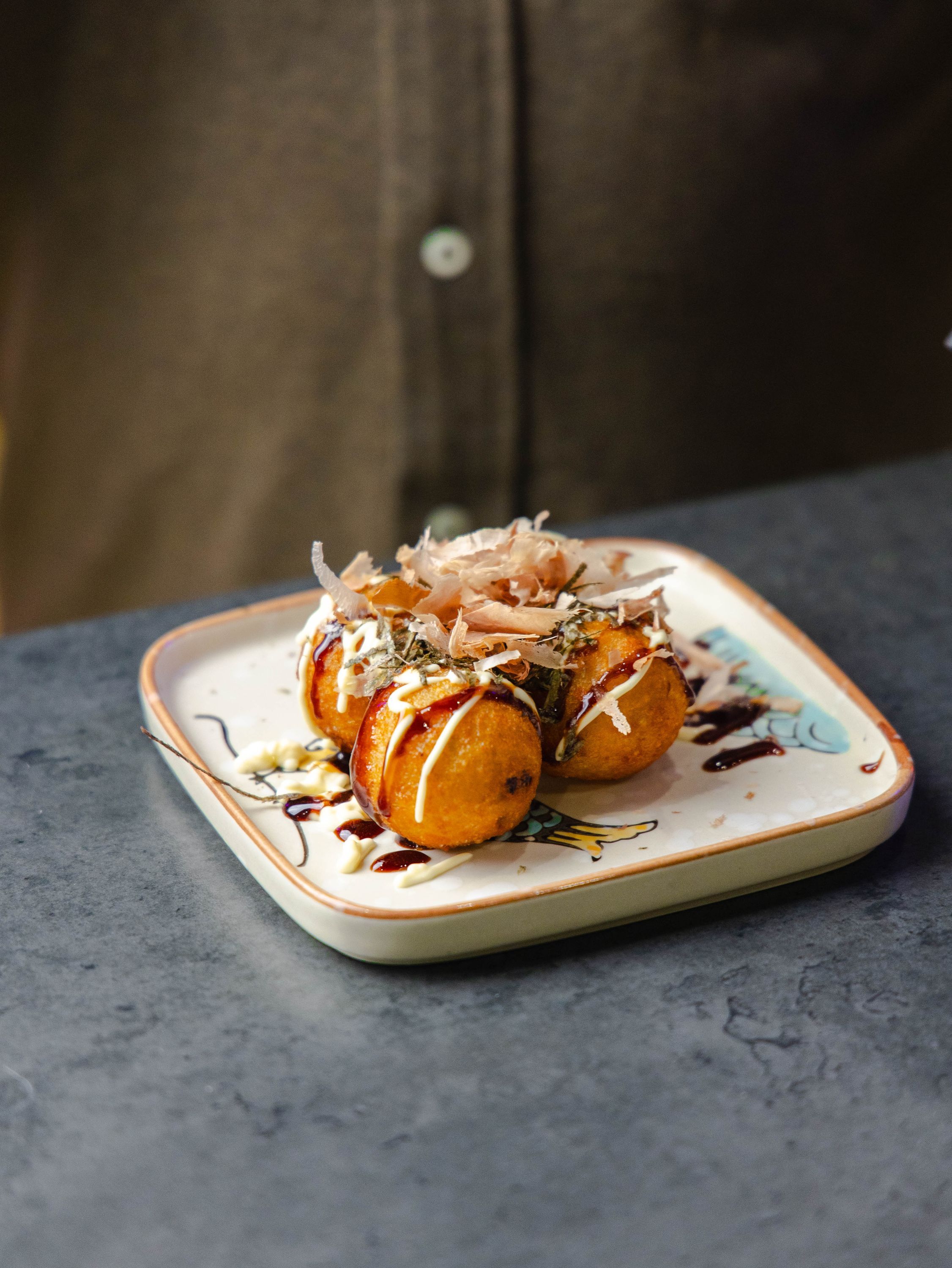 Boulette de takoyaki garnie de flocons de bonite, présentée sur une assiette décorative.