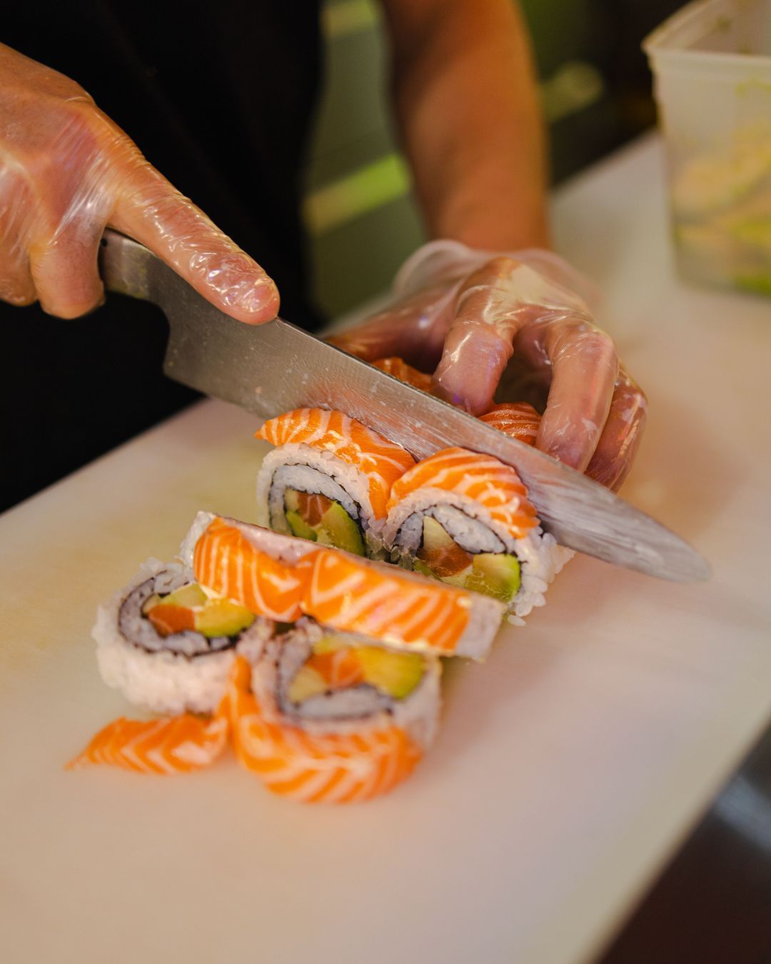 Un chef prépare des sushis avec du saumon et des légumes, mettant en avant des rouleaux frais.